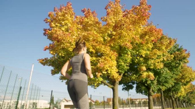 低角度，特写: 适合年轻女子沿着风景秀丽的秋季彩色大道慢跑。