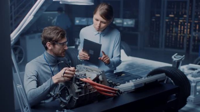 拥有平板电脑和检查工具的男性和女性汽车工程师在使用概念车底盘的高科技实验室中测试电动发动机时进行了交