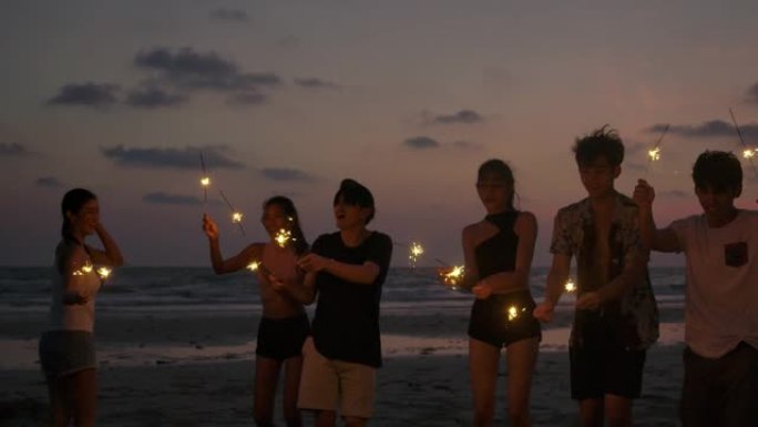 一群朋友在海边的夜间聚会上玩得开心，手里拿着孟加拉的烟火。青少年在海滩上放烟花聚会。慢动作镜头。