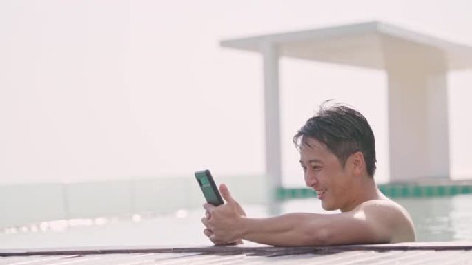 暑假在酒店游泳池用电话的亚洲帅哥。
