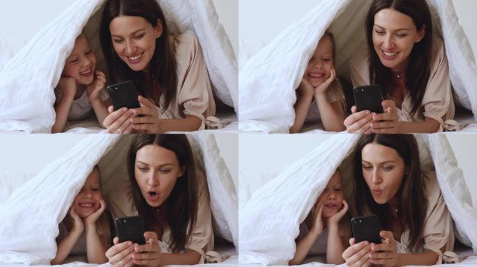 微笑的年轻母亲向快乐的女儿展示有趣的手机应用程序。