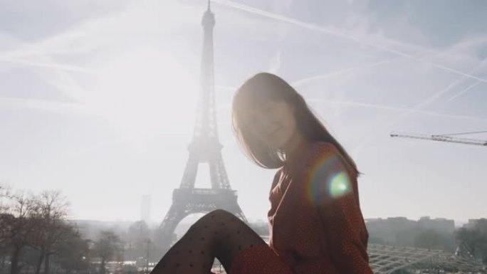 放大美丽的幸福女人微笑着，穿着红色连衣裙坐在史诗般的日落巴黎埃菲尔铁塔上慢动作