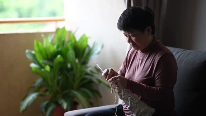 一名亚洲中国中年妇女在业余休闲活动中在客厅编织