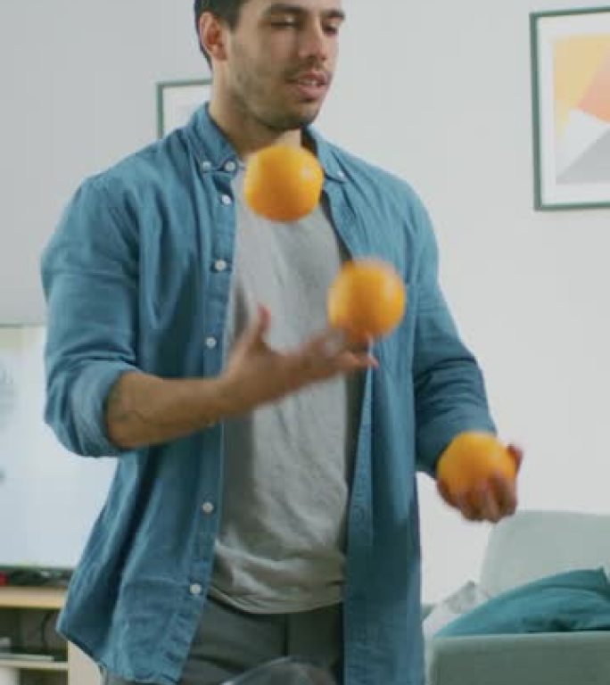 英俊的年轻人在客厅里玩弄橘子，为他的大性能训练。垂直屏幕方向9:16的视频素材