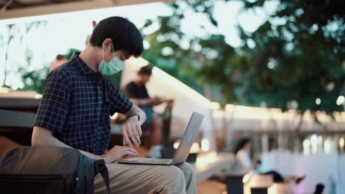 亚洲男子戴着卫生面具，在社交距离的同时工作