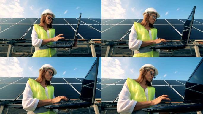 迷人的女专家正站在一块巨大的太阳能电池前，操作一台笔记本电脑