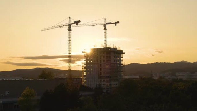 无人机: 金色的日落照亮了绿色小镇上正在建造的摩天大楼