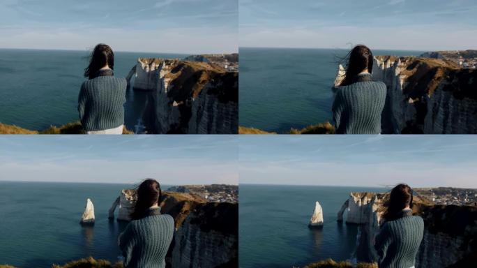 背景拍摄，兴奋的女游客看着华丽的埃特雷塔岩石和海洋全景，头发在风中吹动。