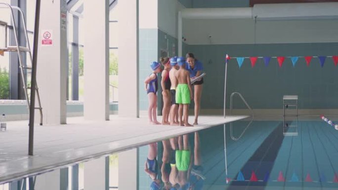 女教练在站在室内游泳池边缘的游泳课简报中给孩子们