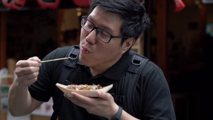 亚洲旅游男子吃章鱼烧，球形日本小吃时感觉很热
