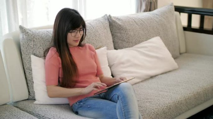 年轻女子在家放松时在沙发上使用数字平板电脑，慢动作