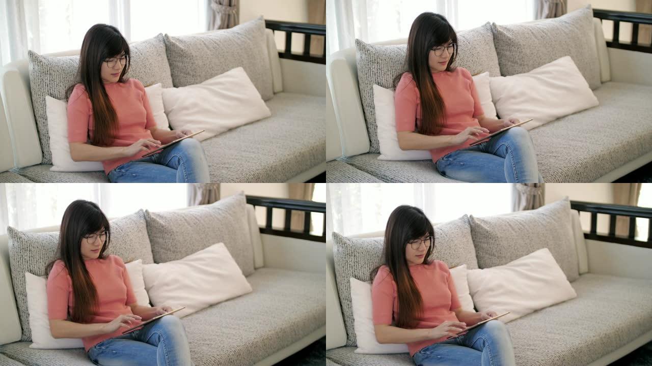 年轻女子在家放松时在沙发上使用数字平板电脑，慢动作