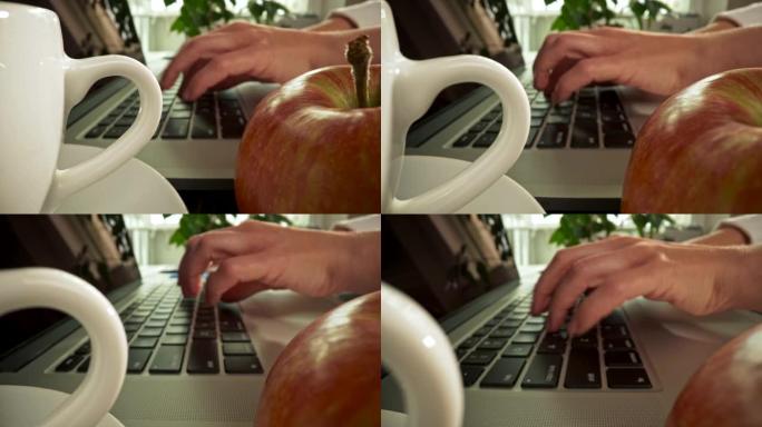 休息一下。热饮和一个红苹果等待忙碌的家庭工作人员喝酒和吃。女性手在笔记本电脑上打字。滑块镜头，4K