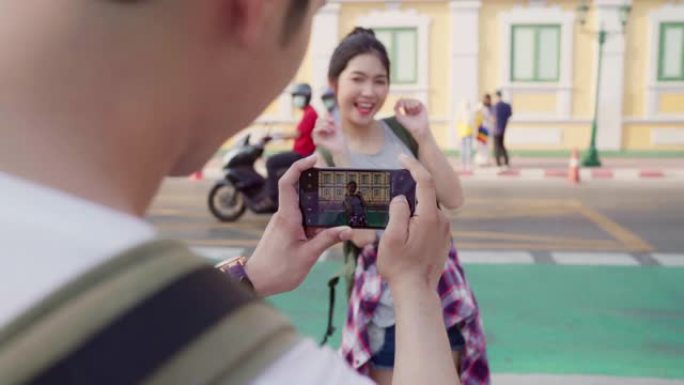 旅行者亚洲夫妇在泰国曼谷旅行，甜蜜的夫妇在日落时利用手机在街道附近互相拍照。生活方式夫妇在城市概念中