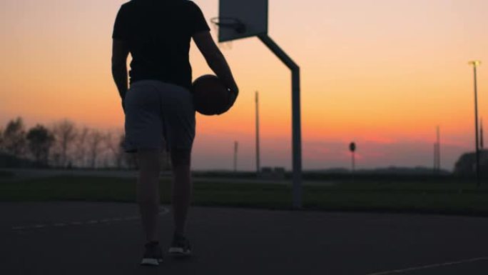 黄昏时分，带着篮球的年轻人走出室外篮球场