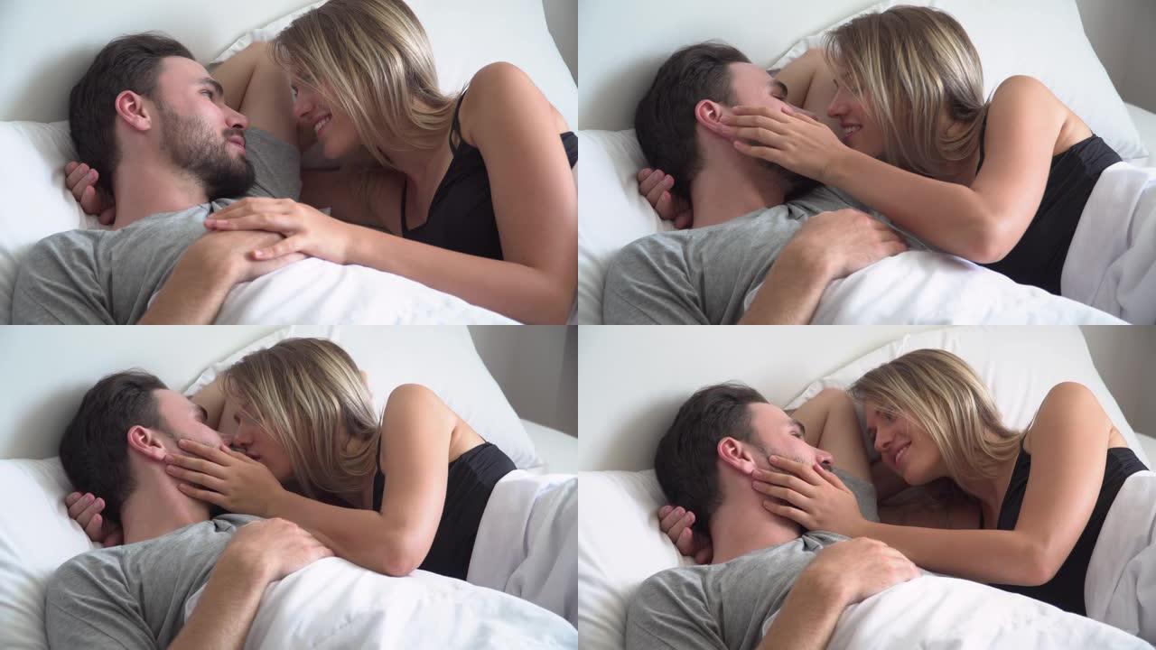 年轻夫妇躺在床上说话和亲吻