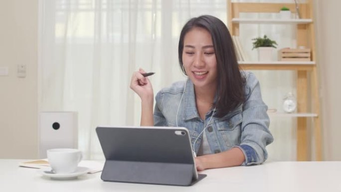 亚洲自由职业商务女性休闲服使用平板电脑工作电话视频会议，客户在客厅在家。