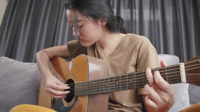 亚洲年轻女孩在家里玩原声吉他和学习在线课程。青少年使用笔记本电脑搜索音乐笔记，在冠状病毒或新型冠状病