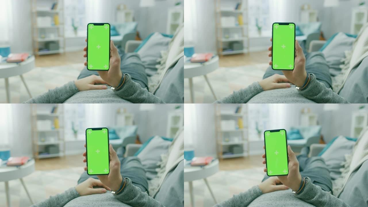 在家中的男子躺在沙发上，使用带有绿色模拟屏幕的智能手机，进行滑动，滚动手势。屏幕上有跟踪标记。视点摄