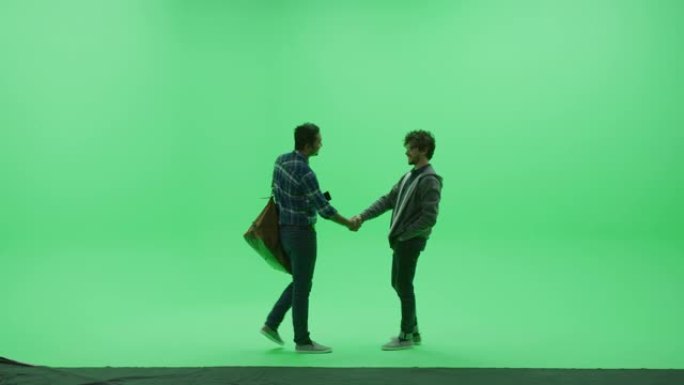 绿屏工作室: 两个年轻英俊的朋友见面，握手问候，并分别走过色键室。侧视图摄像机拍摄