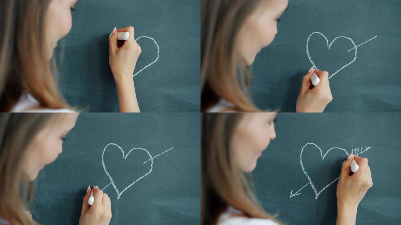 美丽女孩的慢动作用粉笔在黑板上微笑着画心脏图像