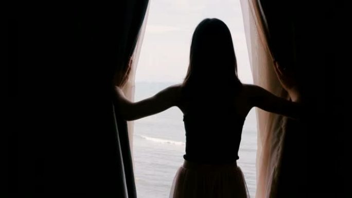 后视图年轻快乐的女人走到打开黑暗的酒店公寓房间的窗帘，享受史诗般的海景慢动作。