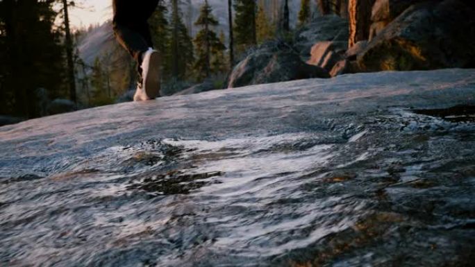 女性的腿跳过一条小水流的后视图，女孩在优胜美地公园慢动作走到岩石边缘。