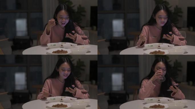 一位亚洲华裔女性在餐厅独自在家用餐，她的智能手机与红酒一起享用