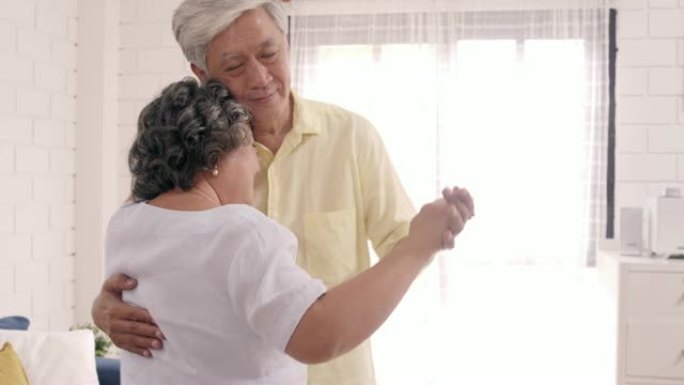 亚洲老年夫妇在家里的客厅里听音乐时一起跳舞，甜蜜的夫妇在家里放松时享受爱情的同时享受乐趣。生活方式老