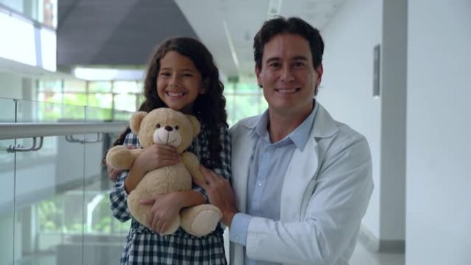快乐的女孩，医院里的医生抱着一只泰迪熊，然后两人都笑着看着相机