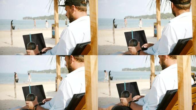 后视图拍摄的成功放松男性自由职业者与水果饮料使用笔记本电脑在夏季度假躺椅上。