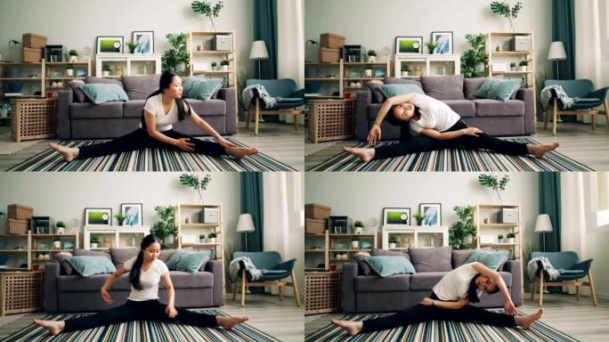 美丽的年轻女士正在家里做体育锻炼，伸展腿和身体坐在时尚现代公寓的地板上。体育和千禧一代的概念。