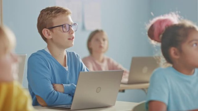 小学计算机科学课: 聪明的男孩使用笔记本电脑，他的同学使用笔记本电脑，每个人都专心听老师的话。儿童接