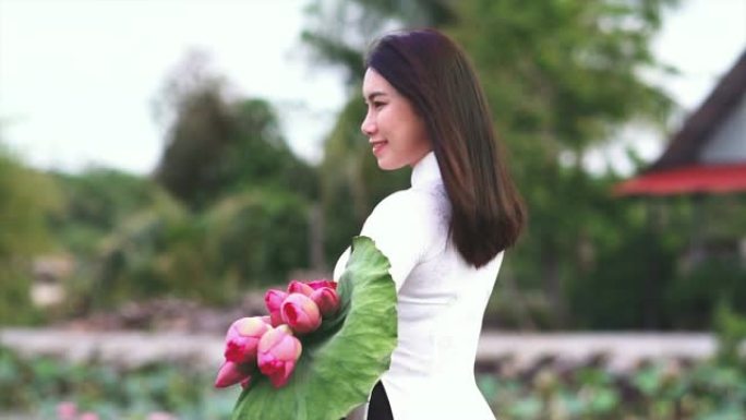 4k慢动作镜头越南美女的肖像拿着粉红色的莲花并在大莲花湖的木桥上获得新鲜空气，越南，亚洲或东南亚旅行