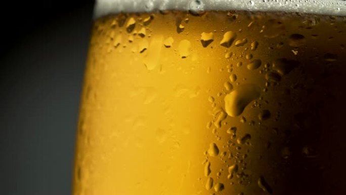 用冷凝水和水滴在玻璃中制作轻啤酒。在黑暗背景上旋转。4K UHD