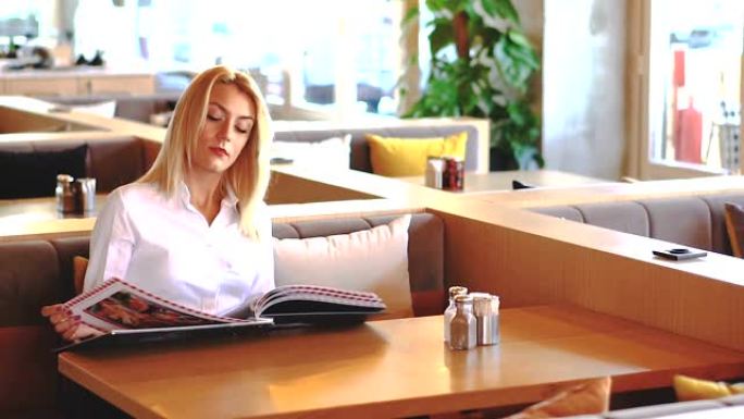 年轻漂亮的女人坐在餐馆或咖啡馆里，看着菜单。