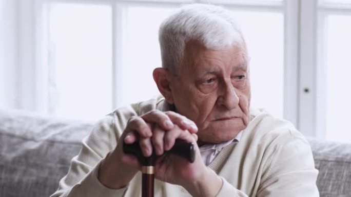 悲伤的老祖父拿着手杖独自坐在沙发上