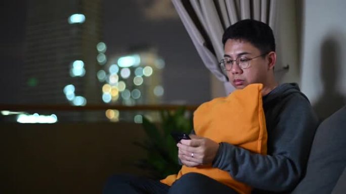一个亚洲华人中年成年人晚上在黑暗中独自在家看电影，戴着耳机和游戏控制器