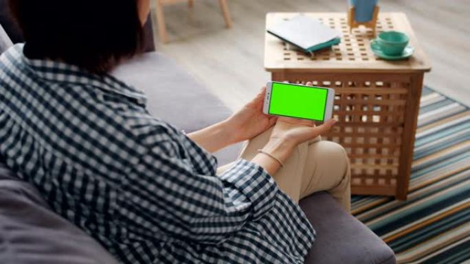 女孩看着坐在家里沙发上的智能手机的绿色模拟屏幕