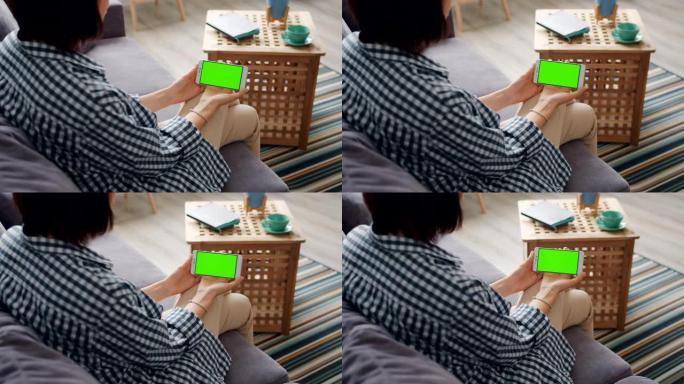 女孩看着坐在家里沙发上的智能手机的绿色模拟屏幕
