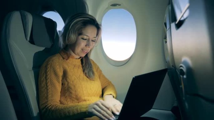 一位女士在飞机上使用笔记本电脑，微笑着。在飞机内工作的女乘客。