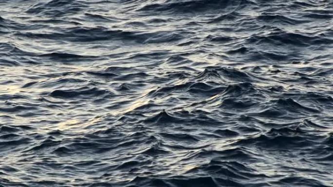 小风暴开始时海水上的波浪。漫射的阳光反射在黑暗的水面上。慢动作抽象镜头