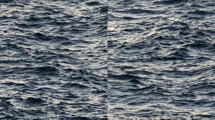小风暴开始时海水上的波浪。漫射的阳光反射在黑暗的水面上。慢动作抽象镜头