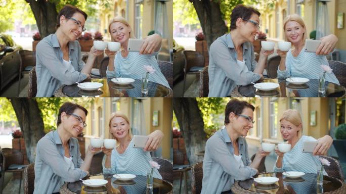 成熟的女士在露天咖啡馆用杯子自拍，拿着咖啡微笑