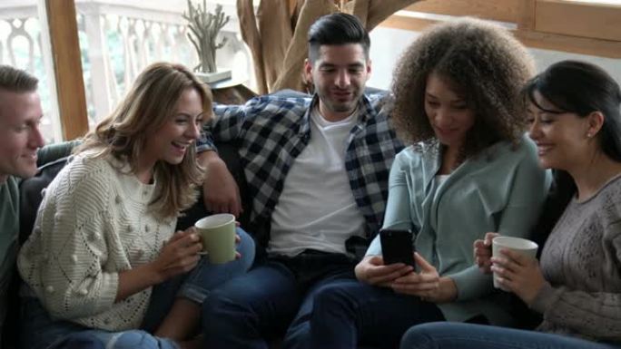 一群多种族的朋友在聊天和喝咖啡的同时在智能手机上观看视频