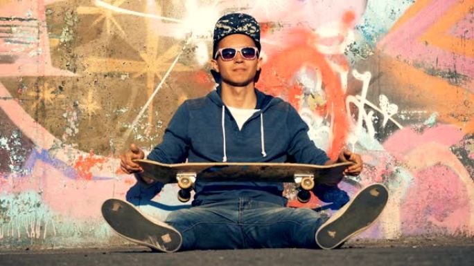 一个微笑的溜冰者坐在涂鸦墙旁边时扭动木板