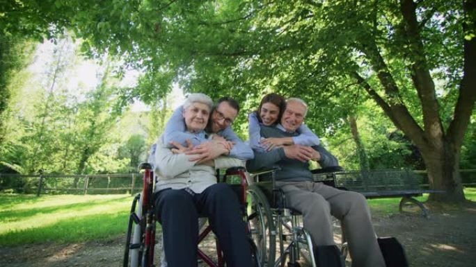 在阳光明媚的日子里，在绿色公园里，快乐的孙子孙女的慢动作拥抱着他们的祖父母，这是爱与尊重的标志。