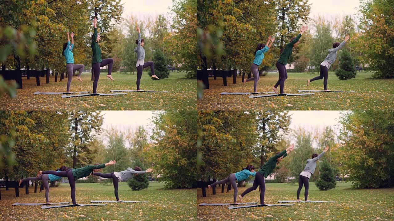 三个苗条女孩在公园做瑜伽的侧视图，练习平衡练习，单腿站在垫子上，移动手臂和身体。青春、休闲和爱好概念