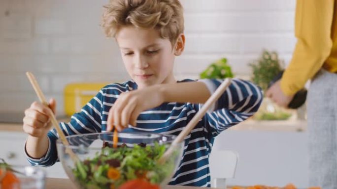 在厨房: 母亲和可爱的小男孩一起烹饪健康的晚餐。妈妈教小儿子健康的习惯，以及如何在沙拉碗中混合蔬菜。