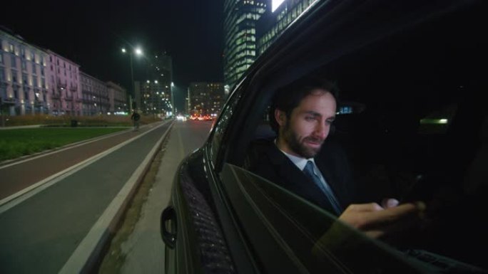 英俊的商人在夜间与城市中心的司机一起乘坐现代汽车旅行时使用笔记本电脑的慢动作。